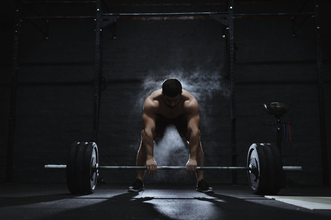 Exhausted male powerlifter gripping a loaded barbell in a dark gym, chalk dust in the air, moments before a heavy deadlift.