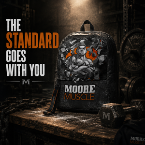 MooreMuscle Performance Backpack displayed under a spotlight on a wooden table inside a dark industrial strength gym.