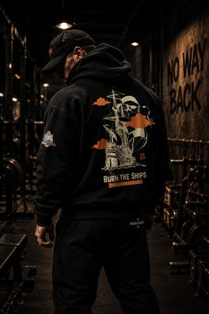 Rear view of the black MooreMuscle Burn The Ships oversized hoodie in a dark urban alley with cinematic lighting and detailed back graphic.
