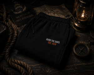 Burn The Ships heavyweight fleece sweatpants displayed on a vintage nautical chart with lantern light, rope, and maritime exploration gear.
