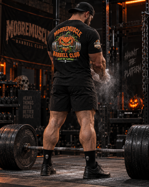 Powerlifter wearing the MMBC Halloween Tee 2026 while chalking up before a deadlift, Haunt the Platform back print visible