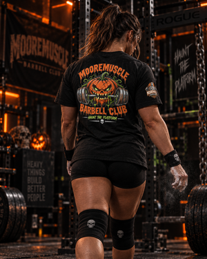 Woman walking away in the MMBC Halloween Tee 2026 with chalked hands, Haunt the Platform pumpkin skull design on the back