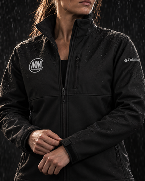 Close-up of a woman in the black MooreMuscle Columbia soft shell jacket in the rain, showing the embroidered MM chest logo and Columbia sleeve logo