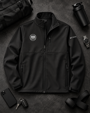 Flat lay of the black MooreMuscle Columbia soft shell jacket with a shaker bottle and gym gear on a dark surface