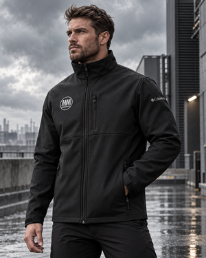 Man in a black MooreMuscle Columbia soft shell jacket standing outdoors on a rainy, overcast day