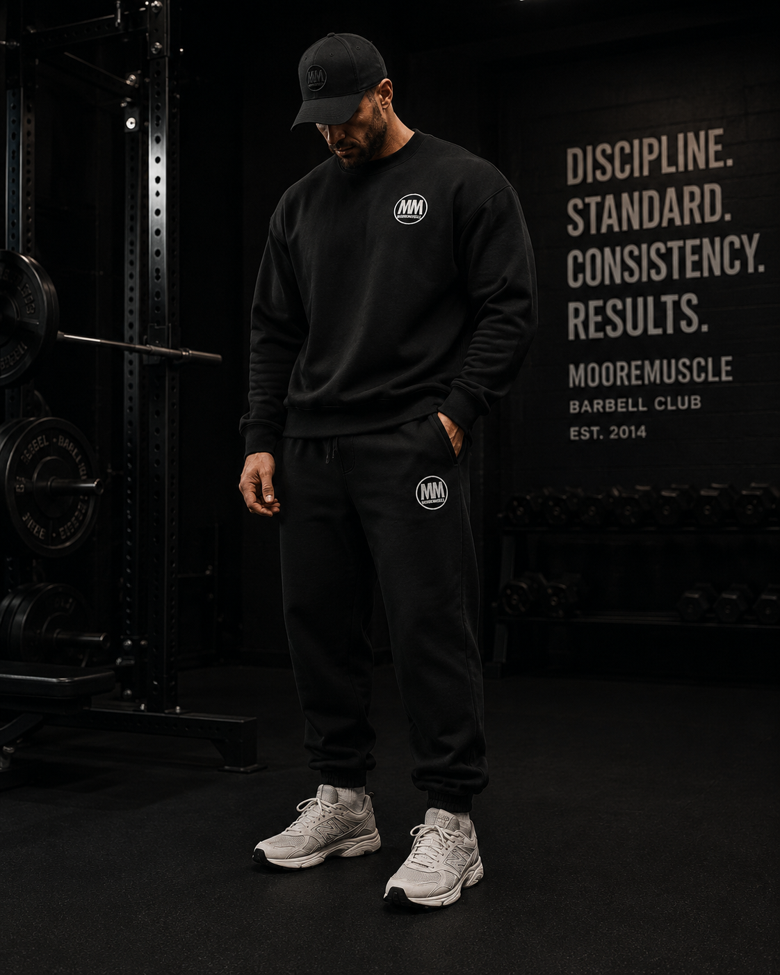 Person wearing a black crewneck with a MM logo, standing in front of a gym wall with 'MooreMuscle' branding.