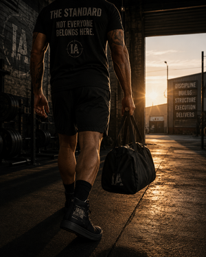 Athlete wearing Iron Architect apparel and high-top shoes walking into a warehouse gym at sunrise carrying training gear.