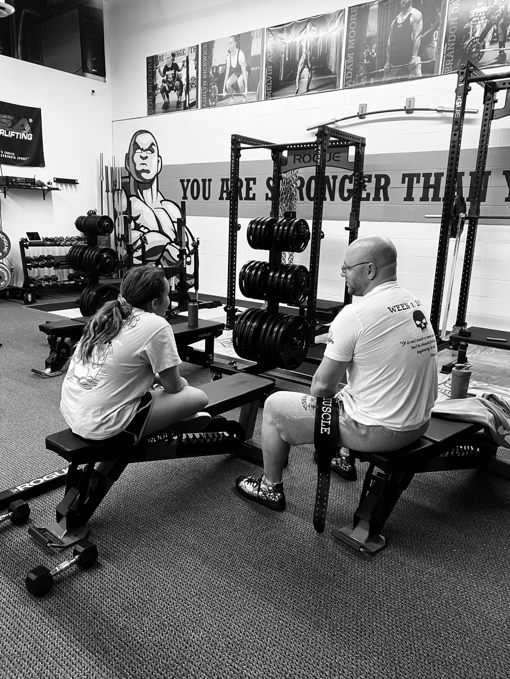Black and white photo of lifters and coaches sitting inside the MooreMuscle training environment
