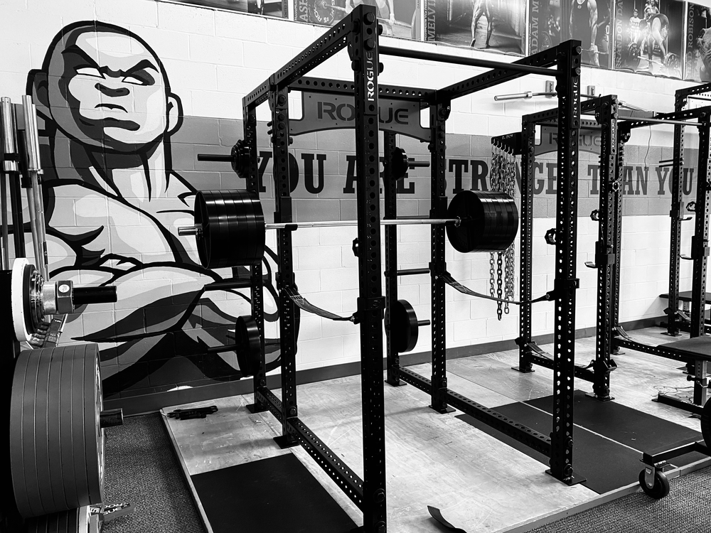 Black and white photo of MooreMuscle racks, platforms, plates, and gym mural