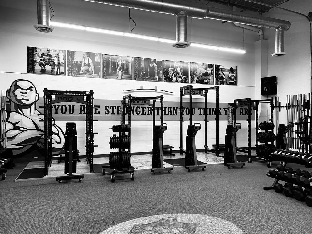 Black and white photo of the MooreMuscle training room with racks, platforms, and strength equipment