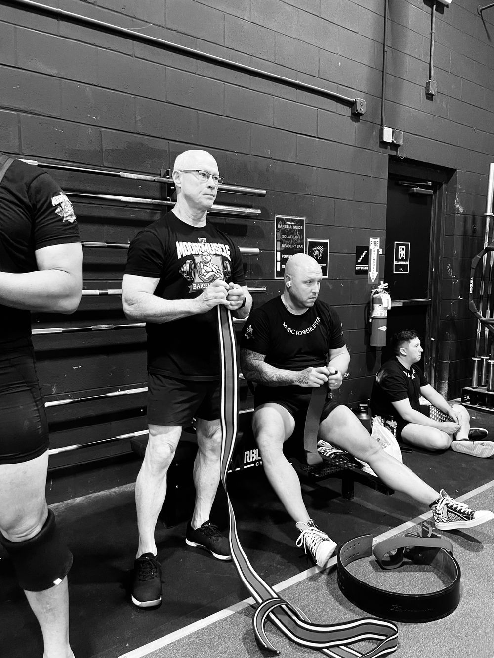 Black and white photo of lifters preparing for powerlifting inside the gym