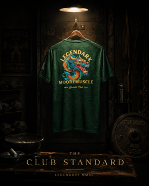 Green MooreMuscle Legendary Tee displayed under a spotlight inside a dark powerlifting gym.
