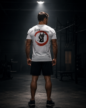 Athlete standing alone under a single gym light wearing the white Never Surrender tee with the back graphic visible.