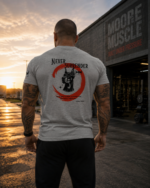 Male athlete standing outside a gym at sunrise wearing the Never Surrender athletic gray tee with Doberman back graphic.