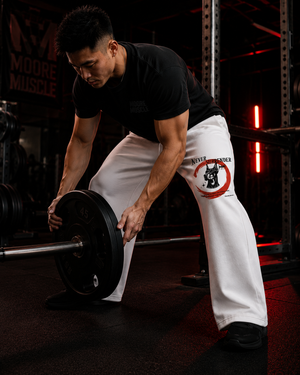 Person lifting a barbell in a gym setting wearing Never Surrender white sweatpants