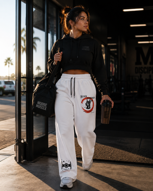 Woman in black hoodie and white Never Surrender sweatpants walking outside a building.