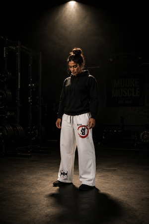 Person wearing a black hoodie and white Never Surrender pants with a logo in a dark setting