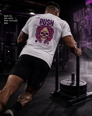 Athlete wearing the Push Your Limits Tri-Blend Tee while pushing a heavily loaded sled in a dark gym.