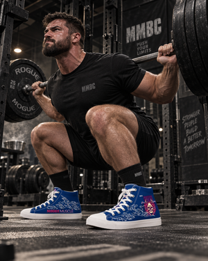 Male powerlifter squatting in blue MooreMuscle Push Your Limits high-top training shoes inside a powerlifting gym.