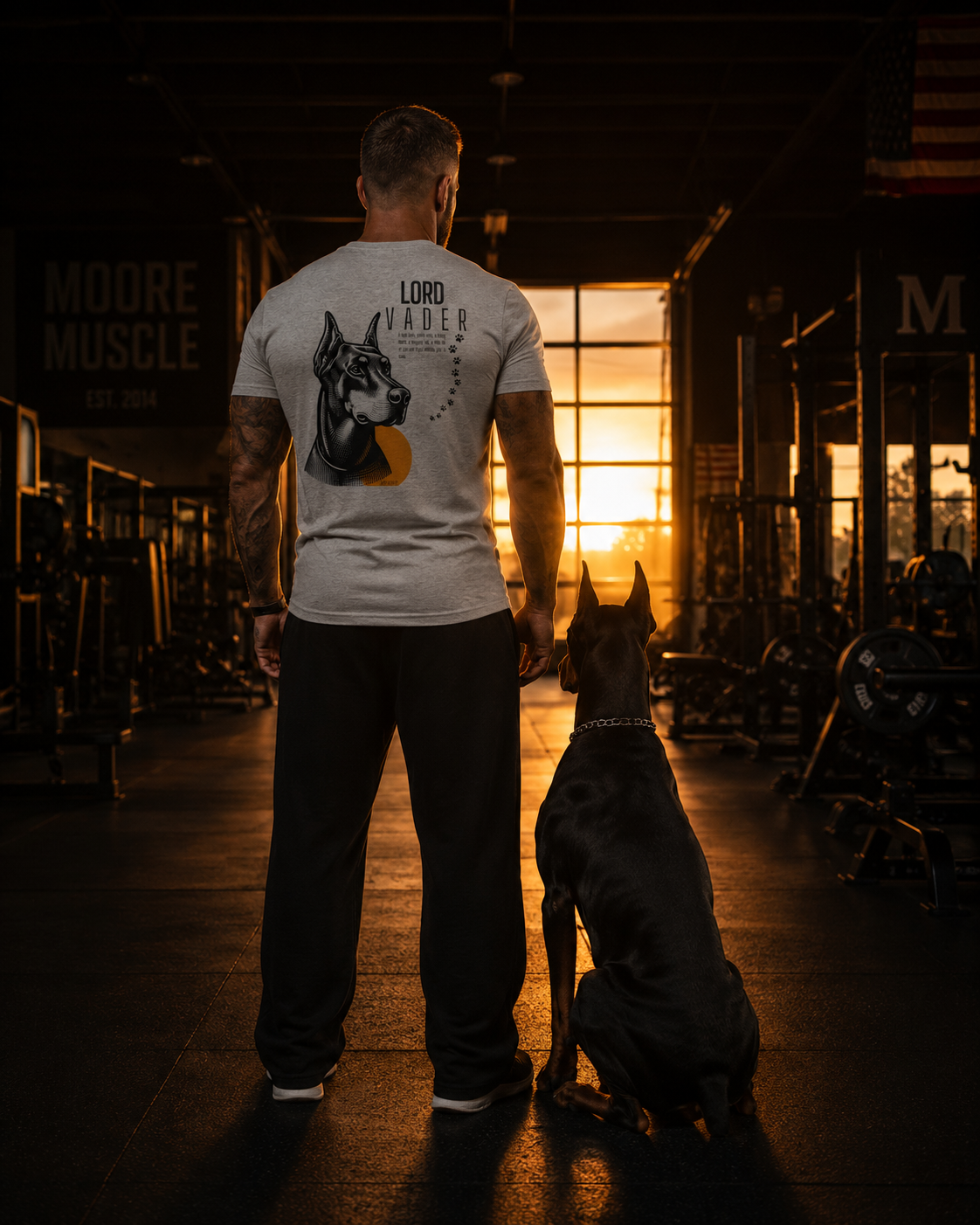 Lord Vader memorial tri-blend tee worn by an athlete standing beside a Doberman in a quiet gym at sunset.