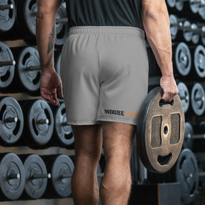Strength athlete walking through gym holding weight plate while wearing MooreMuscle Day of the Deadlift training shorts