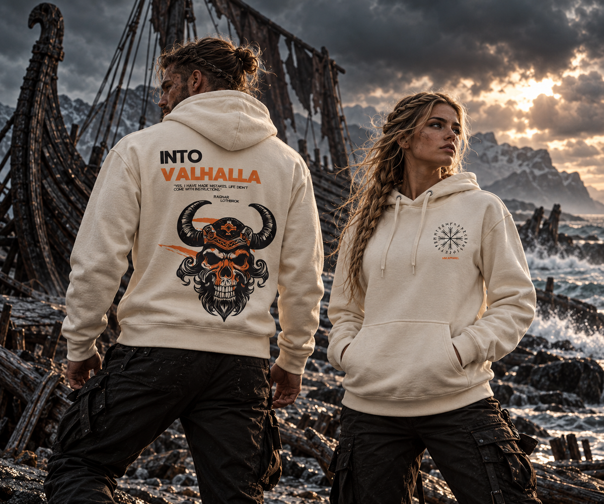 Man and woman wearing the MooreMuscle Into Valhalla hoodie in bone among Viking shipwrecks, showing the horned skull back graphic and compass chest logo