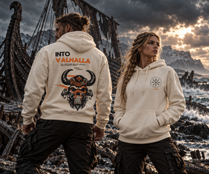 Man and woman wearing the MooreMuscle Into Valhalla hoodie in bone among Viking shipwrecks, showing the horned skull back graphic and compass chest logo