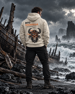 Man on a stormy coast beside a wrecked Viking ship, back view of the Into Valhalla hoodie graphic in orange and black