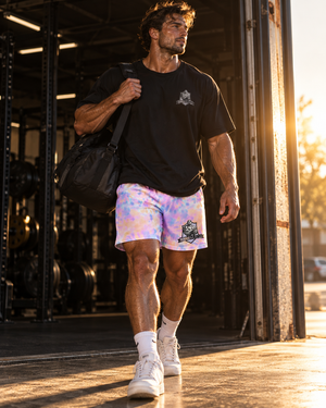 Male athlete carrying a gym bag at sunset in MooreMuscle Afterglow pastel training shorts and a black MooreMuscle tee
