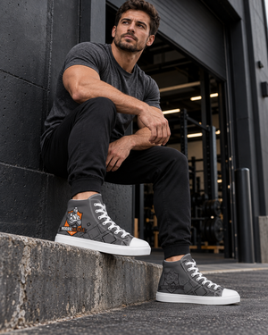 Man seated in a gym doorway wearing grey MooreMuscle Crest canvas high tops with white soles and the orange shield logo