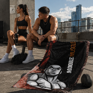 MooreMuscle grunge beach towel draped over concrete block with visible fabric texture and wrinkles, featuring bold black, red, and white graphic design in a dark studio setting