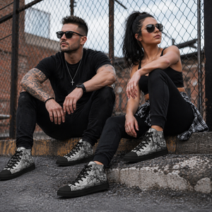 Male and female athletes wearing MooreMuscle black high top skull design sneakers sitting on an urban curb in a gritty industrial setting, showcasing black soles and laces lifestyle view