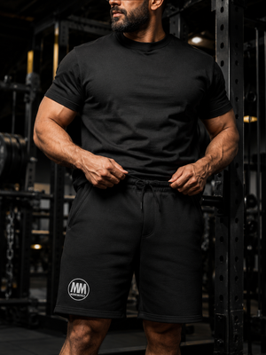 Close-up of a man adjusting the drawstring waistband on black MooreMuscle fleece shorts, embroidered MM logo on the leg
