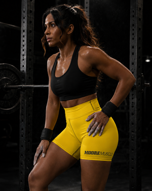 Side view of a woman in yellow MooreMuscle Squat High-Waist Compression Shorts with the MooreMuscle logo on the hip