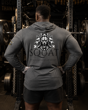 Man wearing the MooreMuscle Squat Hooded Long-Sleeve Tee, back view, showing the three-headed wolf SQUAT graphic in a gym power rack