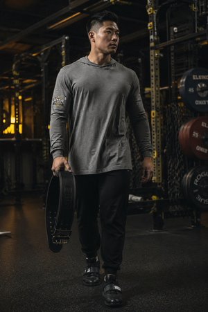 Man wearing the MooreMuscle Squat Hooded Long-Sleeve Tee, front view, walking through the gym holding a lifting belt