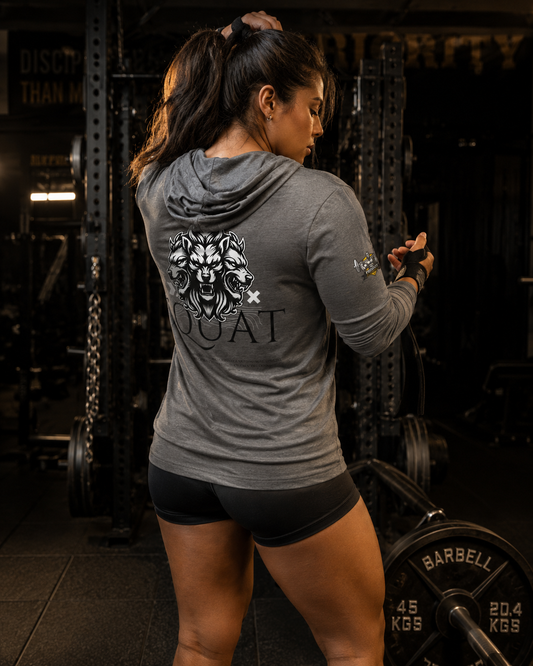 Woman wearing the MooreMuscle Squat Hooded Long-Sleeve Tee, back view, tying her hair up beside a loaded barbell