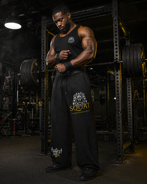 Man wearing black MooreMuscle Squat Sweatpants with lion and SQUAT graphic, wrapping wrist wraps in a gym power rack