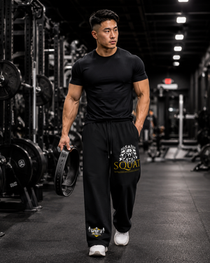 Man walking through a gym aisle in black MooreMuscle Squat Sweatpants holding a rolled lifting belt