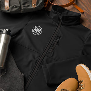 Close-up of black MooreMuscle Columbia soft shell jacket showing chest zipper pocket, fabric texture, and embroidered logo.